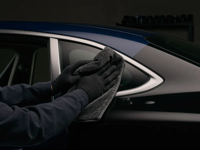 Behandschuhte Hände polieren mit einem Mikrofasertuch eine Fahrzeugtür